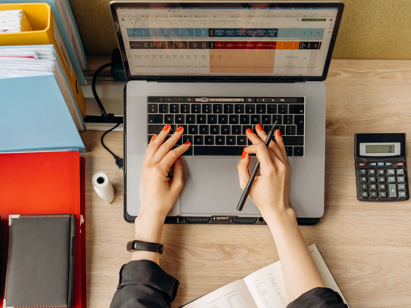 Hands typing on a laptop with a spreadsheet, next to folders and a calculator